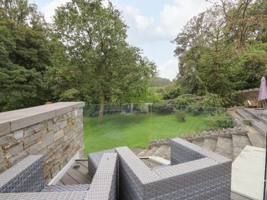 An outdoor patio with gray wicker furniture glass railing stone steps and green lawn with trees at Glamorgan House in Cardiff
