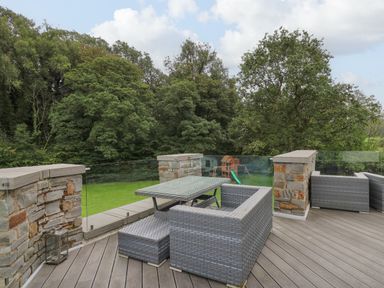 An outdoor patio with wicker furniture and glass table overlooking a grassy yard with trees and a wooden playset at Glamorgan House in Cardiff
