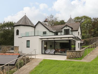 An exterior view of a two story house with turrets glass railings and a patio with two chairs at Glamorgan House in Cardiff