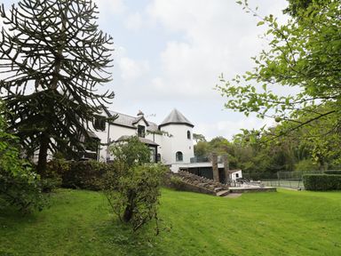 A large white house with a turret surrounded by trees and a lawn with a tennis court in the background at Glamorgan House Cardiff