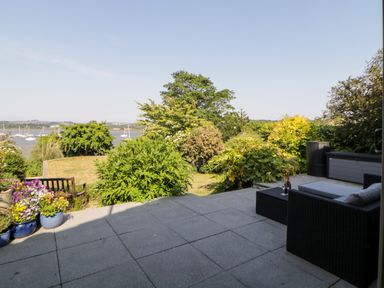 An outdoor patio with garden furniture and plants overlooking a body of water with sailboats at Riverview @ 1 Brunel View in Saltash