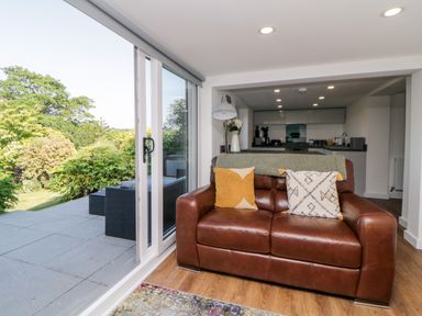 A living room with a brown leather sofa and sliding glass doors opening to a garden at Riverview @ 1 Brunel View Saltash