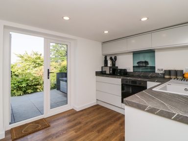 A kitchen with white cabinets gray countertops and wooden floor with glass door leading outside at Riverview @ 1 Brunel View Saltash