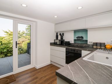 A kitchen with white cabinets a black oven a gray countertop a white sink and glass door leading outside at Riverview @ 1 Brunel View Saltash
