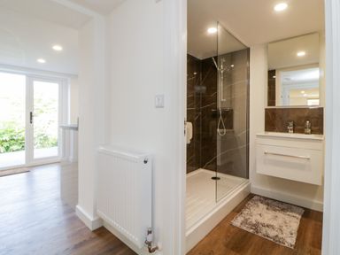 A bathroom with a glass shower enclosure a sink with a mirror and a rug beside wooden flooring at Riverview 1 Brunel View in Saltash