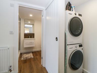 A hallway with stacked washer and dryer next to a sliding door leading to a bathroom with a sink and mirror at Riverview @ 1 Brunel View in Saltash
