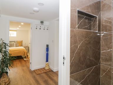 A hallway with a plant and umbrella stand leading to a bedroom and a tiled bathroom at Riverview @ 1 Brunel View in Saltash