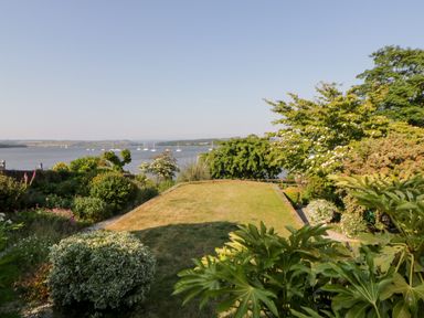 A garden with grass and various shrubs overlooking a body of water with sailboats at Riverview @ 1 Brunel View in Saltash