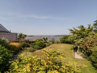 A garden with trees and bushes overlooking a body of water with boats at Riverview @ 1 Brunel View in Saltash