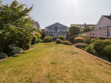 A large backyard with green lawn bushes and shrubs and a two story house at Riverview @ 1 Brunel View in Saltash
