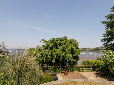An outdoor deck with seating and greenery overlooking a river with boats at Riverview @ 1 Brunel View in Saltash