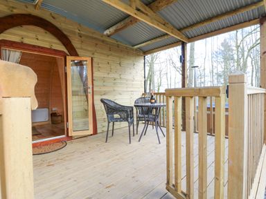 An outdoor wooden deck with a round table and two chairs bottle and glasses on the table at The Leveret in Eppleby
