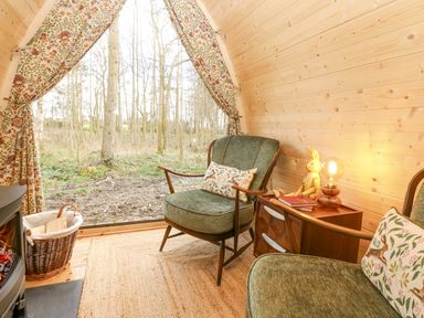 A small wooden room with green armchairs a woven rug and a basket of firewood at The Leveret in Eppleby