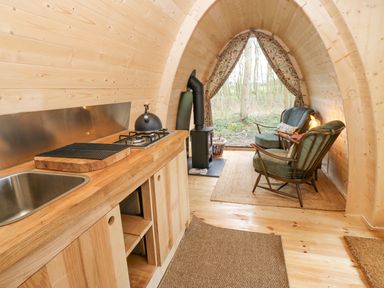 A small wooden cabin interior with a kitchenette and two chairs near a stove at The Leveret in Eppleby