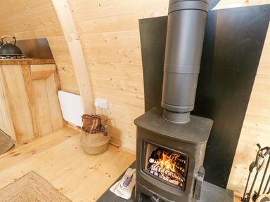 A wood burning stove with fire inside next to a basket with a blanket and gloves in a wooden room at The Leveret in Eppleby