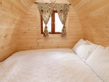A small bedroom with wood-paneled walls a window with floral curtains and a bed with white bedding at The Leveret in Eppleby