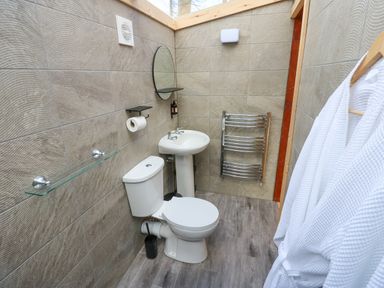 A bathroom with a toilet sink round mirror towel rack and bathrobes hanging at The Leveret in Eppleby