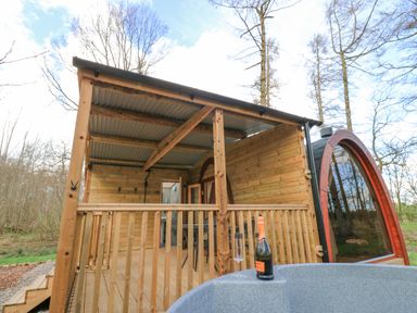 A wooden outdoor deck with a roof and railing next to a hot tub with a bottle and glass at The Leveret in Eppleby