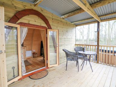 An outdoor wooden porch with two wicker chairs and a round table next to an open wood cabin door at The Leveret in Eppleby