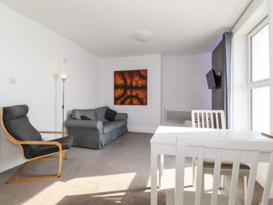 A living room with a gray sofa black armchair white dining table and chairs and wall art at Apartment 9 Beaconsfield House in Bridlington