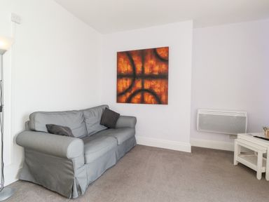 A living room with a grey sofa two dark cushions and an abstract wall art at Apartment 9 Beaconsfield House in Bridlington