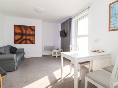 A living room with a gray sofa a white dining table and chairs a wall-mounted television and abstract paintings at Apartment 9 Beaconsfield House in Bridlington