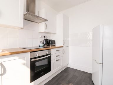 A kitchen with white cabinets a built in oven a stove a kettle a toaster and a refrigerator at Apartment 9 Beaconsfield House in Bridlington