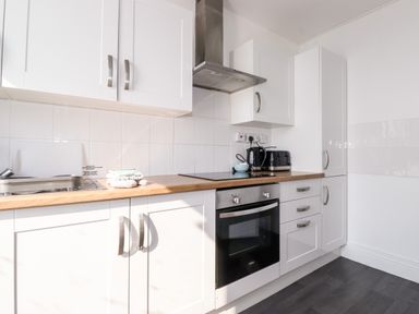 A kitchen with white cabinets a wooden countertop an oven a stovetop a stainless steel sink a kettle a toaster and a stainless steel extractor hood at Apartment 9 Beaconsfield House in Bridlington