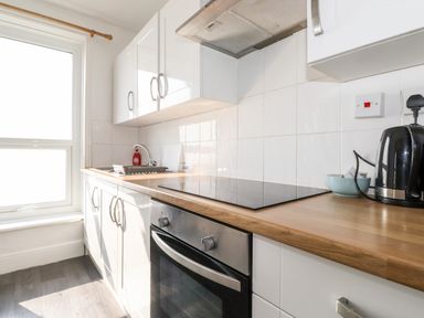 A kitchen with white cabinets a wooden countertop an electric stove an oven a sink a kettle and a window at Apartment 9 Beaconsfield House in Bridlington