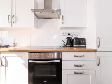 A kitchen with a built-in oven stovetop extractor hood white cabinets black toaster and kettle at Apartment 9 Beaconsfield House in Bridlington