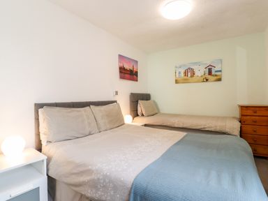 A bedroom with a double bed and a single bed with nightstands and lamps and a wooden chest of drawers at Apartment 9 Beaconsfield House in Bridlington