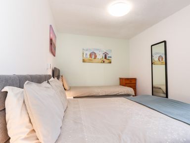 A bedroom with two beds a wooden dresser a mirror and paintings on the walls at Apartment 9 Beaconsfield House in Bridlington