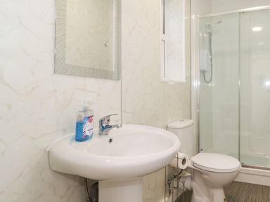 A bathroom with a sink, mirror, toilet, toilet paper holder, and glass enclosed shower at Apartment 9 Beaconsfield House Bridlington
