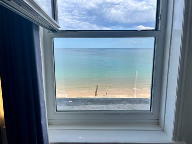 A beach view through a closed window with part of a blue curtain on the left at Apartment 9 Beaconsfield House in Bridlington