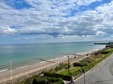 A view of a beach with calm sea water a promenade with railings and streetlights and a road with greenery at Apartment 9 Beaconsfield House Bridlington