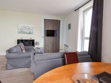 A living room with gray sofas a round wooden table and a wall-mounted TV at 7 Beach View Beaconsfield House in Bridlington
