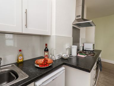 A kitchen countertop with a loaf of bread, tomatoes, a bottle of wine, two wine glasses, a kettle, microwave, stove, and a sink at 7 Beach View Beaconsfield House in Bridlington