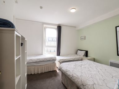 A bedroom with three single beds a window with curtains and a white shelf unit at 7 Beach View @ Beaconsfield House in Bridlington