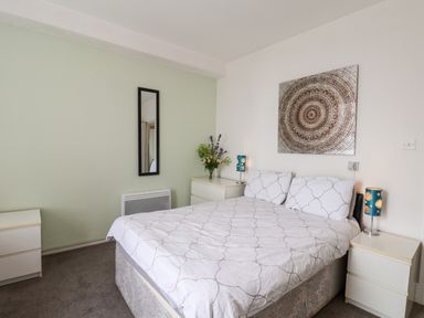 A bedroom with a double bed two bedside tables with lamps wall art a mirror and a chest of drawers with flowers at 7 Beach View Beaconsfield House Bridlington