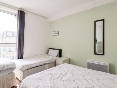 A bedroom with two single beds a nightstand a mirror on the wall and a window with curtains at 7 Beach View Beaconsfield House in Bridlington