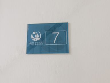 A blue sign with the number 7 and Beaconsfield Holiday Apartments logo on a white wall at 7 Beach View at Beaconsfield House in Bridlington