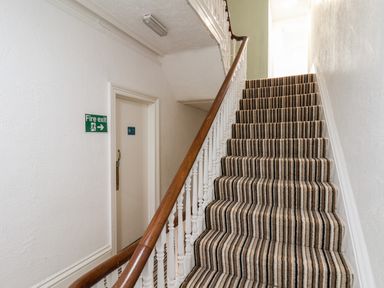 A staircase with striped carpet next to a door with a fire exit sign at 7 Beach View Beaconsfield House in Bridlington