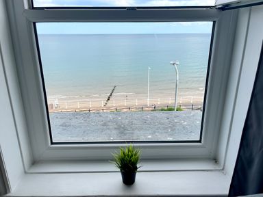 A window overlooking a beach and sea with a small potted plant on the windowsill at 7 Beach View @ Beaconsfield House Bridlington
