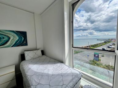 A bedroom with a single bed next to a large window showing a seaside view at 7 Beach View Beaconsfield House in Bridlington