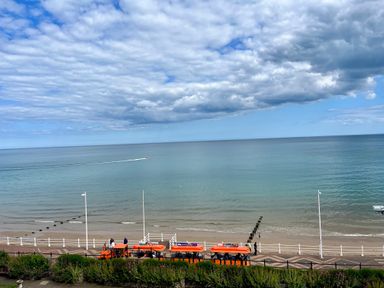 A beach with a calm sea under a partly cloudy sky with orange tourist vehicles parked on a promenade at 7 Beach View @ Beaconsfield House in Bridlington