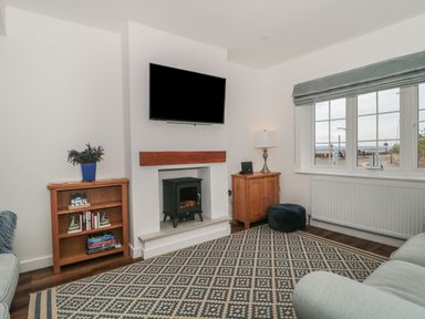 A living room with a TV above a fireplace and bookshelves by the walls at Quay Cottage Sea View in Poole