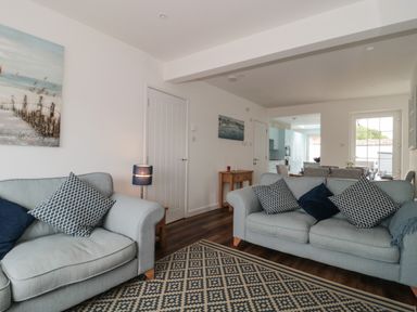 A living room with two grey sofas and patterned cushions a side table with a lamp and a dining area visible at Quay Cottage - Sea View Poole