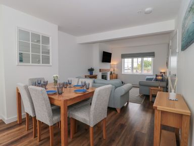 A dining table with six chairs and tableware next to a living room with two sofas a television and a window at Quay Cottage - Sea View in Poole
