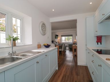 A kitchen with blue cabinets and a double sink overlooking a dining area and living room at Quay Cottage - Sea View in Poole