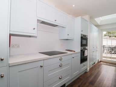A kitchen with light blue cabinets a stovetop double oven wooden floor and glass door leading outside at Quay Cottage Sea View in Poole
